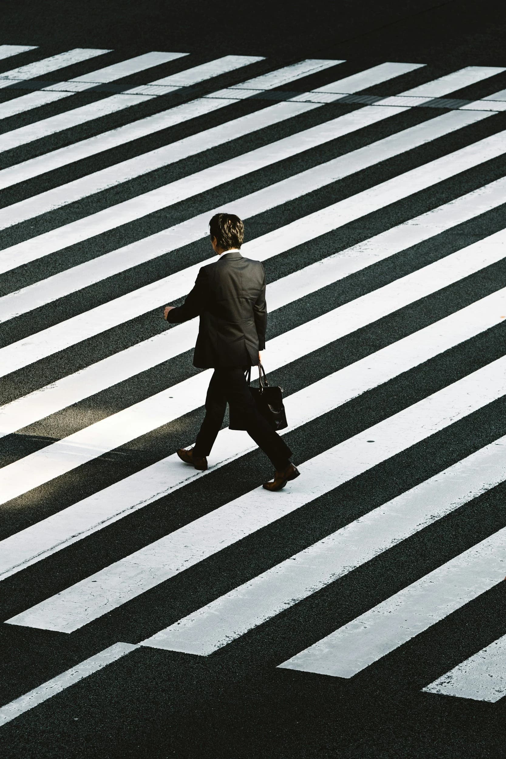 A person in a business suit crossing a zebra crossing carrying a briefcase.