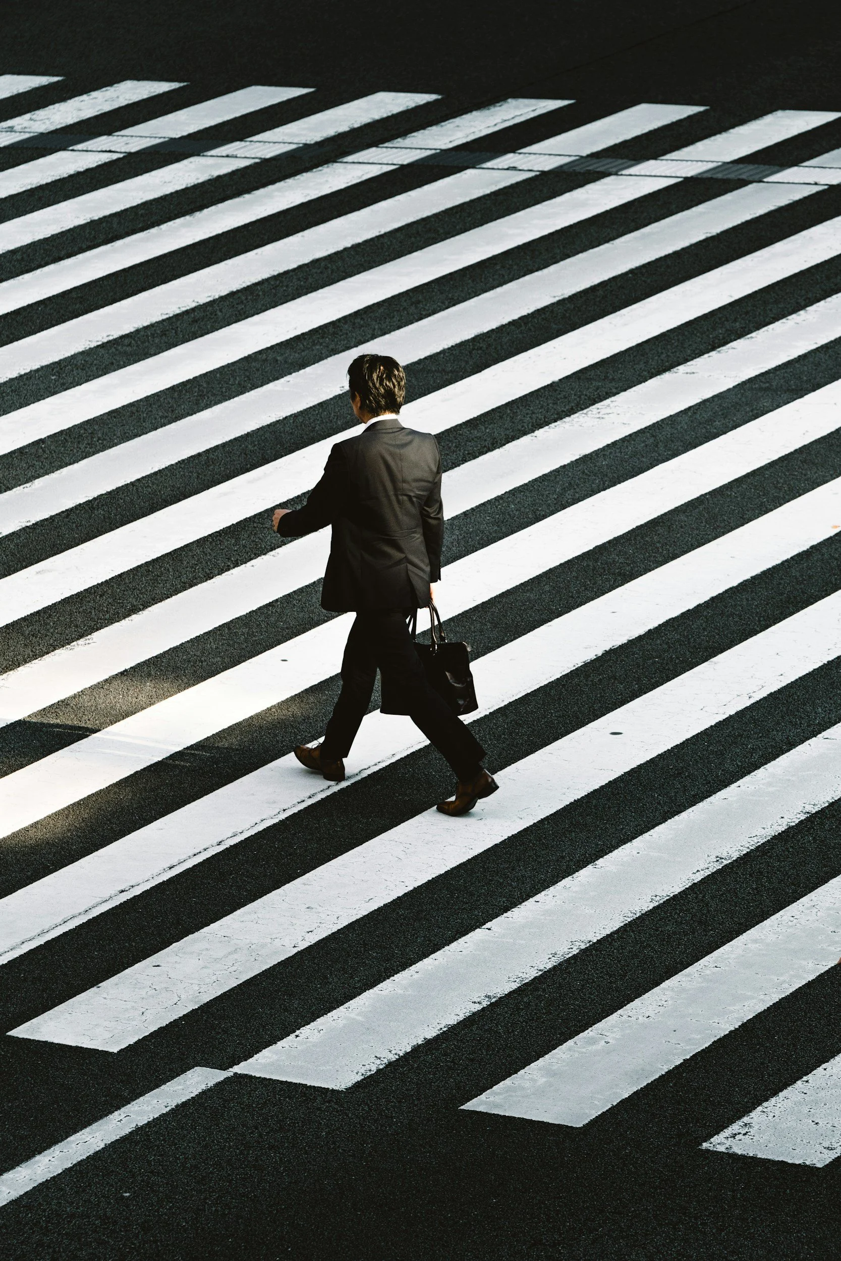 A person in a business suit crossing a zebra crossing on the street while carrying a briefcase.